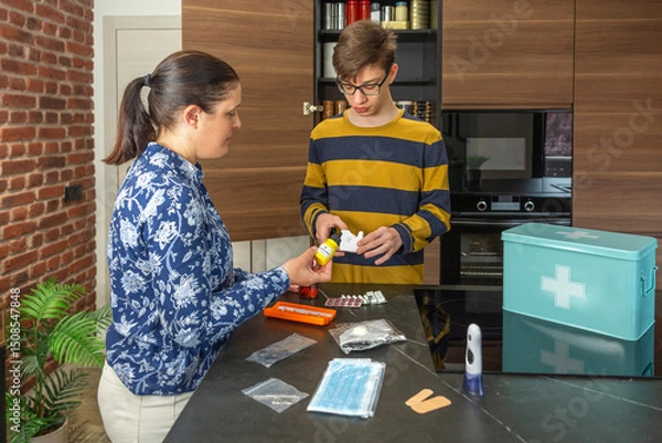 Fototapeta Family preparing 72 hour survival kit and checking medical supplies and medications for emergencies at home. Mother and teenage son organizing self sufficiency strategy, ensuring safety and health.