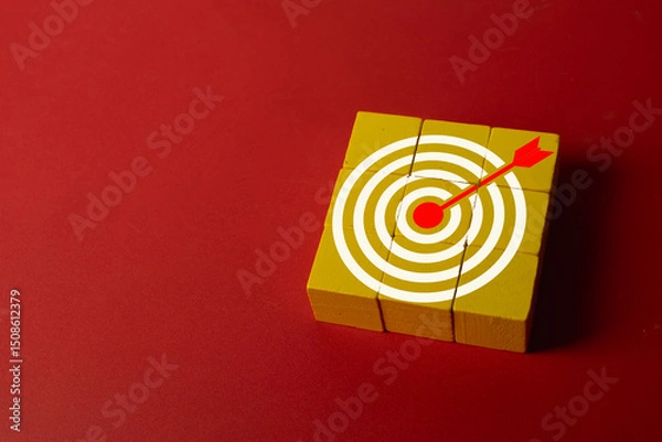 Obraz Concept of achieving goals,goal setting,business success, precision,marketing objectives and strategic targeting.,Red arrow hitting the center of a white target on wooden blocks over red background.