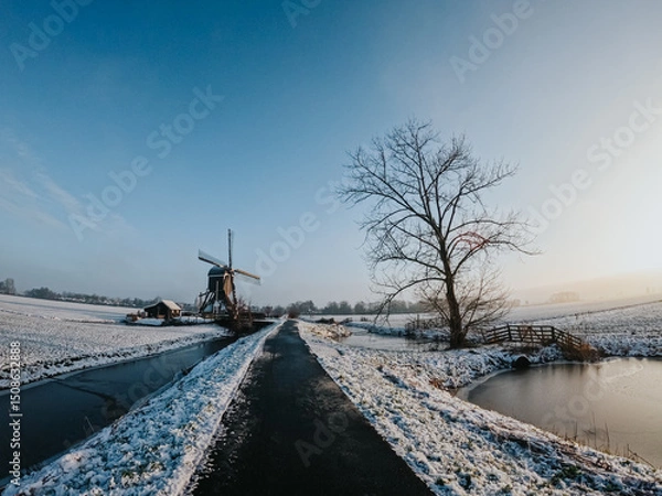 Fototapeta A frozen country road specific to rural Holland during a frosty winter. Walking path along the famous Dutch canals and windmills