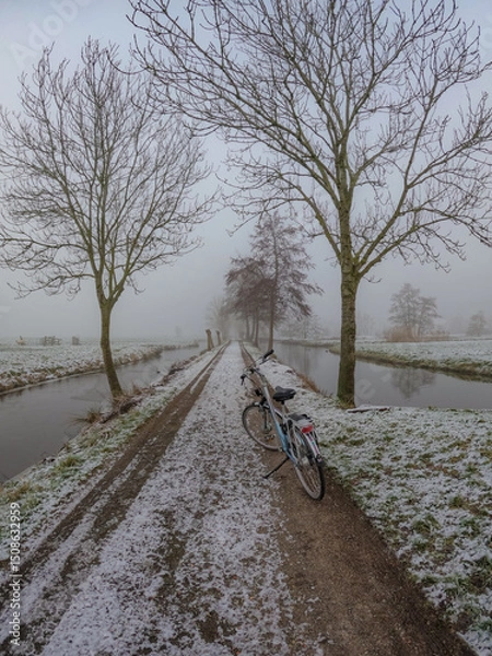 Fototapeta A frozen country road specific to rural Holland during a frosty winter. Walking path along the famous Dutch canals and windmills