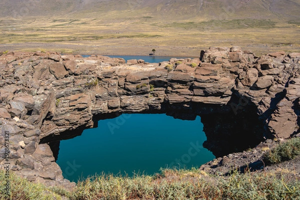 Fototapeta Stone bridge arches over a pool of turquoise water, surrounded by rocky terrain. Caviahue, Neuquen, Argentina