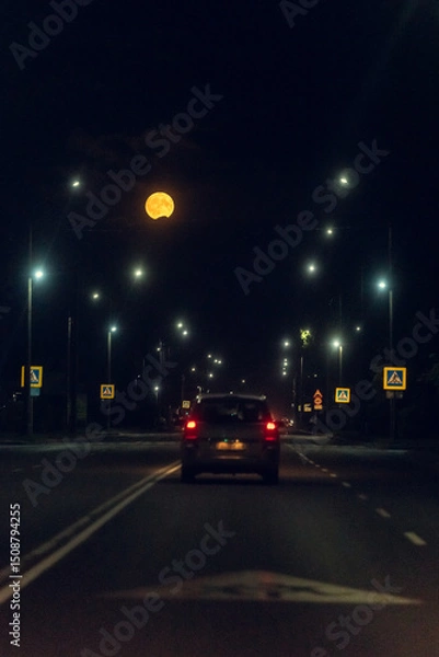 Fototapeta City street late in the evening with beautiful light of lanterns and the moon in the dark sky.