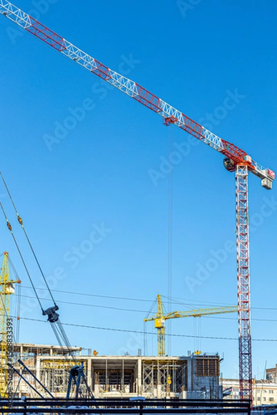 Fototapeta Tall building under construction with scaffolds,Freestanding tower crane on a building site.Building construction site work against blue sky