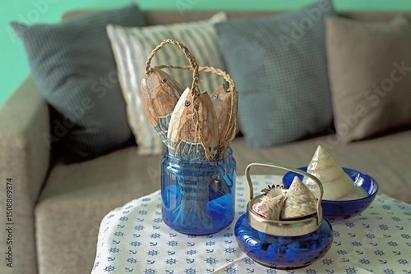 Fototapeta Marine style in the apartment interior - a sofa with pillows and a table with shells and fish figures.