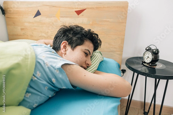 Obraz Teenager girl waking up and looking at alarm clock in bedroom