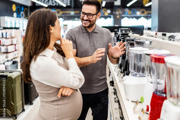Obraz Smiling shop assistant helping a pregnant customer choose home appliances while showcasing various products in a vibrant electronics store