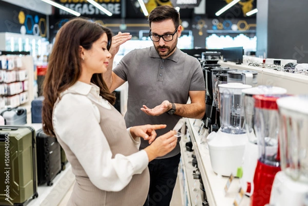 Obraz Smiling shop assistant helping a pregnant customer choose home appliances while showcasing various products in a vibrant electronics store