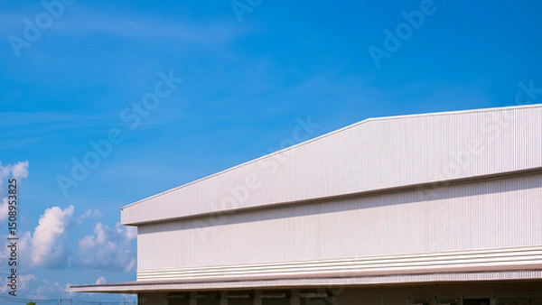 Fototapeta Large Factory Warehouse Industrial Building with Corrugated Metal Awning and Gable Roof against Blue Sky Background, Perspective Side View with Copy space