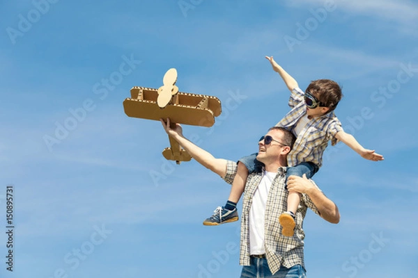 Obraz Father and son playing with cardboard toy airplane in the park at the day time.