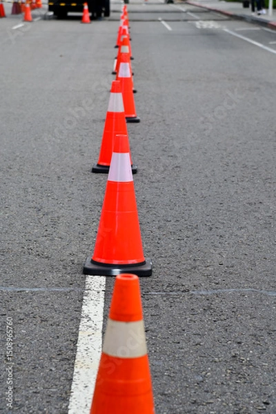 Fototapeta Close-up of the traffic cone on the road. Bright orange traffic cones standing in a row on asphalt. Transportation tool, equipment. Road works. Cityscape.