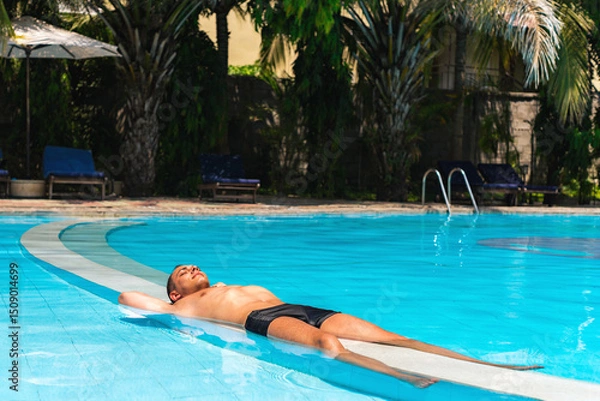 Fototapeta A Man Is Resting In Pool Water At A Resort, Relaxing In The Sunlight On Vacations