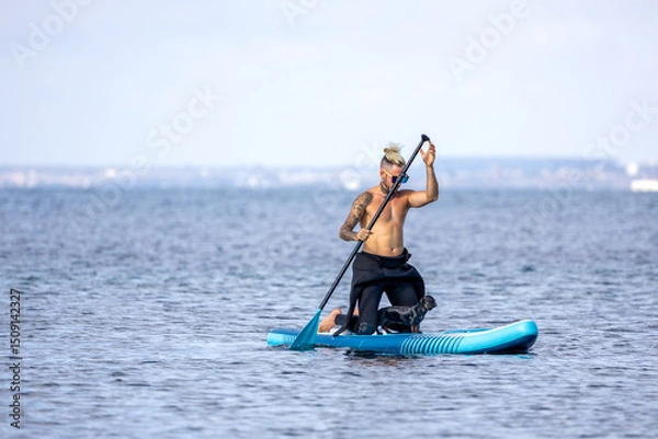 Fototapeta Man paddle surfing with a dog.