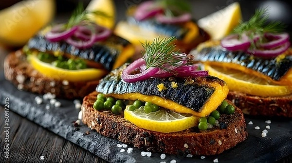 Fototapeta Close up of mackerel open faced sandwiches with lemon peas and red onion on dark bread and slate board