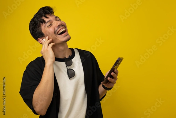 Obraz Young freckled man with a mustache smiling while listening to music with wireless headphones on a yellow background with space for advertising text