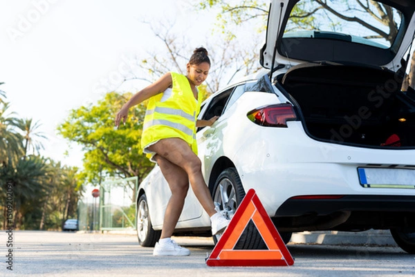 Obraz Woman positioning warning triangle after car breakdown on road