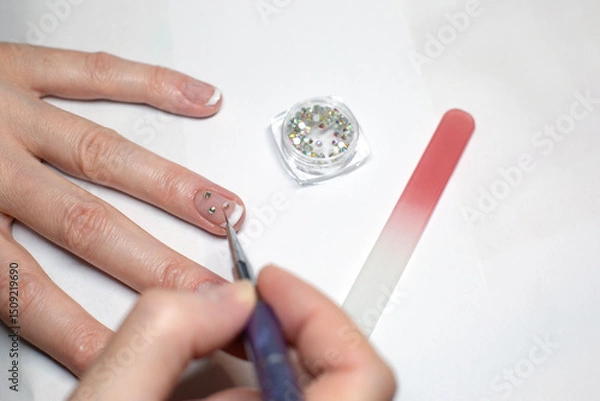 Obraz A woman is doing a manicure, fixing diamond rhinestones on her nails.
