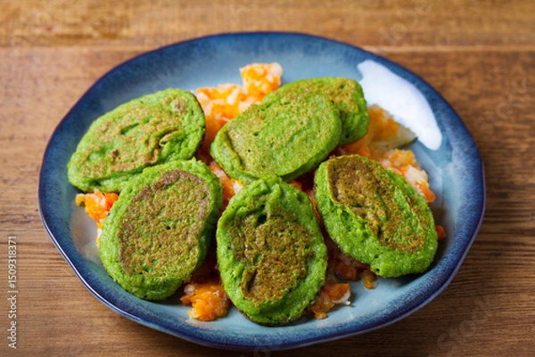 Fototapeta Green pea cakes on mashed carrot and parsnip. Vegetable fritters, pancakes on blue plate