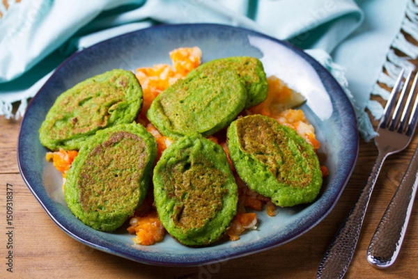 Fototapeta Green pea cakes on mashed carrot and parsnip. Vegetable fritters, pancakes on blue plate