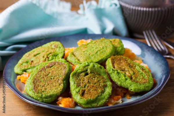 Fototapeta Green pea cakes on mashed carrot and parsnip. Vegetable fritters, pancakes on blue plate