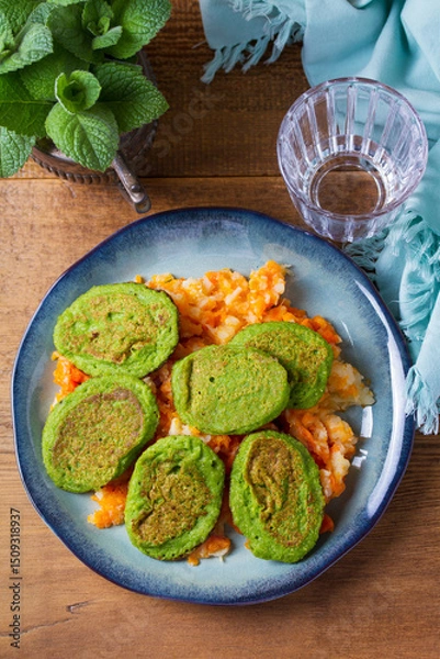 Fototapeta Green pea cakes on mashed carrot and parsnip. Vegetable fritters, pancakes. View from above, top studio shot