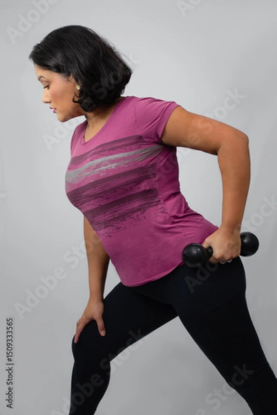 Fototapeta Empowered woman performing weight lifting with dumbbell at studio. Perfect for triceps workout, fitness, strength training. Neutral gray background with copy space.