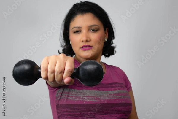 Fototapeta Close up of brunette woman performing weight lifting with dumbbell at studio. Horizontal portrait ideal for workout, fitness, strength training. Gray background, copy space, focus on foreground.