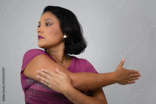 Fototapeta Pretty, serious woman stretching out her arm. Ideal for home workout, exercising, warm-up and fitness classes. Neutral gray background with copy space. Horizontal studio portrait.
