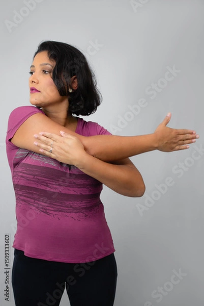 Fototapeta Beautiful, serious woman stretching out her arm. Ideal for home workout, exercising, warm-up and fitness classes. Neutral gray background with copy space.