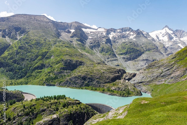 Fototapeta Turquoise Grossglockner glacier reservoir  Speicher Margaritzen alpine slopes and forested hills with concrete dam structure at valley edge. High-altitude lake in vibrant natural mountain scenery