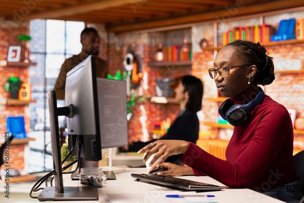 Fototapeta Programmer in startup office using large language model to get help with coding project. African american worker interacting with AI LLM chatbot PC GPT software on PC in software development workplace