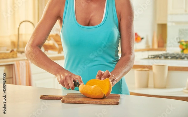 Obraz Manos de mujer con top sin mangas  cortando mango sobre tabla de madera