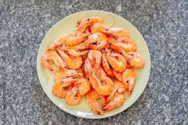 Fototapeta Cooked shrimps are arranged on a light green plate placed on a granite countertop, ready to be enjoyed as a delicious seafood meal or appetizer