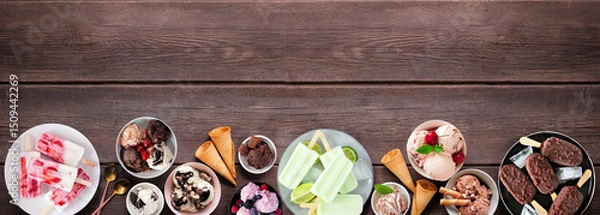 Obraz Cool summer food bottom border. Variety of ice cream bowls, popsicles and frozen treats. Top view on a dark wood banner background. Copy space.