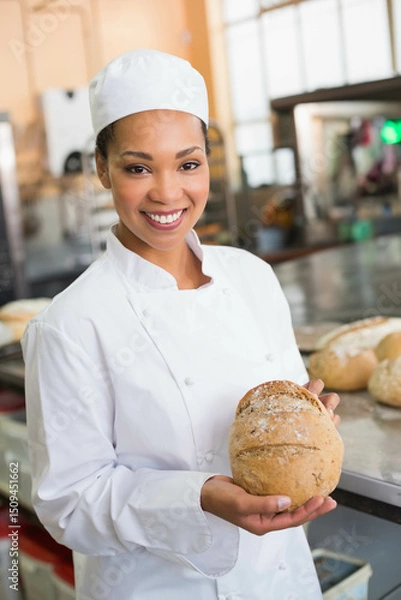 Obraz Baked round loaf resting on stainless steel table in bright bakery kitchen with ovens racks mixers