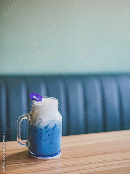 Fototapeta Butterfly pea milk tea. A glass of blue drink milk tea topping with milk foam and a petal of butterfly pea on the wooden table, copy space background for your text. Soft focus.