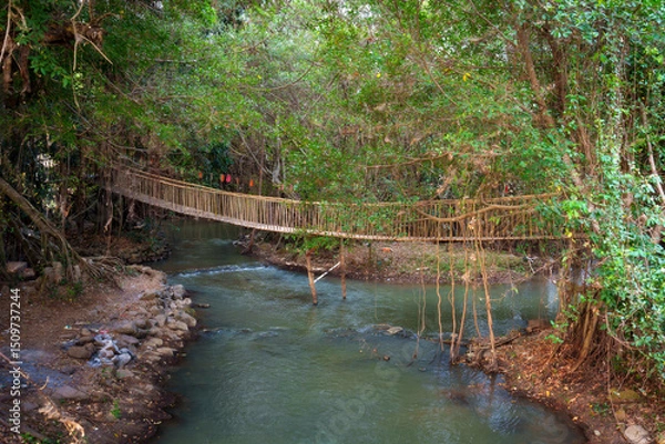 Fototapeta Suspended bridge over tranquil river in Buon Don district, Dak Lak province, Vietnam surrounded by lush greenery