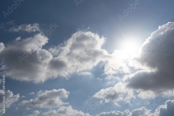 Obraz The sun shines brightly through thick white clouds against a deep blue sky. A dramatic and radiant moment capturing the power and contrast of nature's light.