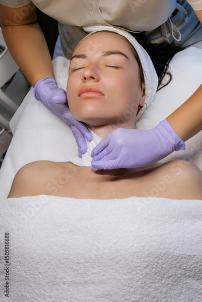 Obraz Esthetician cleansing woman's face with towel after facial treatment in beauty salon, young woman relaxing with closed eyes