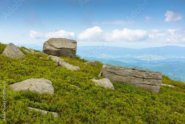 Fototapeta boulder on a hill under blue sky with clouds in summer. huge sandstone among the grass. view in to the distant valley and vihorlat ridge on the horizon