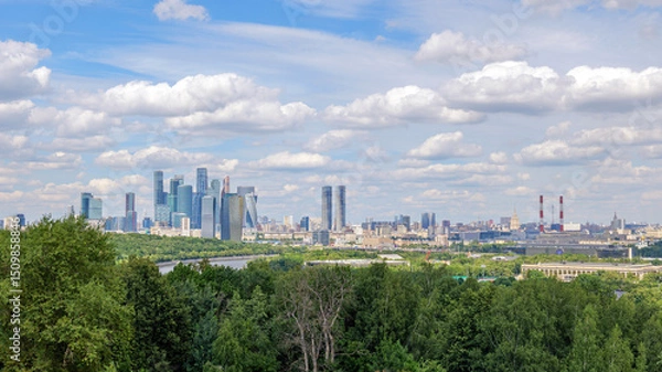 Fototapeta Breathtaking view of Moscow skyline from Vorobyovy Gory, with Moscow River, green trees, and clouds in the blue sky. The Moscow skyline dominates the horizon, creating a stunning scene