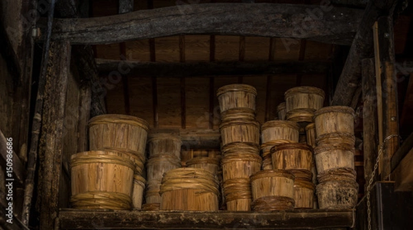 Fototapeta Rows of traditional wooden stake barrels with bamboo hoops wait on the street behind a soy souce brewing factory warehouse in Japan.