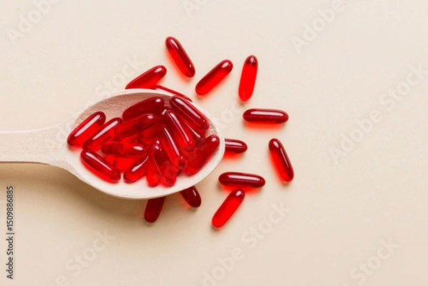 Fototapeta Vitamin capsules in a spoon on a colored background. Pills served as a healthy meal. Red soft gel vitamin supplement capsules on spoon