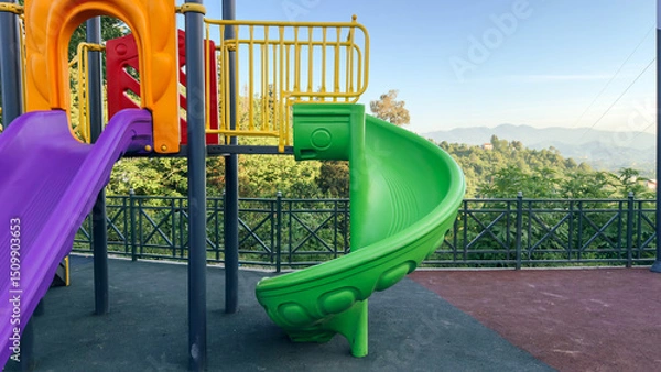 Fototapeta colorful playground slide set against a backdrop of lush green hills and a clear blue sky, offering a fun spot for children with a scenic view