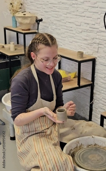 Fototapeta Pottery master class. Teenage girl creates pottery in pottery workshop. Creative process. Hobby and learning concept. a young girl with a bowl of a clay