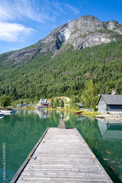 Fototapeta A sunny view of the quiet wooden pier in Loen, Norway, with the Loen Skylift ascending to Mount Hoven in the background, surrounded by majestic fjord landscapes