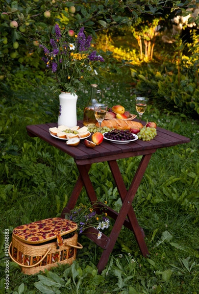 Obraz Romantic picnic setup featuring wine, cheese, and fruits in orchard setting