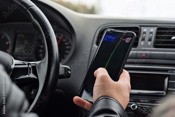 Fototapeta Driver in a black leather jacket checks a navigation app on a smartphone while driving, emphasizing the role of technology in modern road travel.