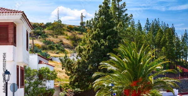 Fototapeta Village street in Artenara with palms, pines, and view of the sacred rock with Christ statue on the hill Gran Canaria, Spain