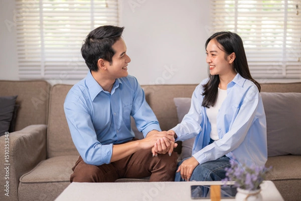 Fototapeta A man and a woman are sitting on a couch, smiling at each other