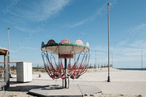 Fototapeta Abandoned carousel on the beach under a blue sky